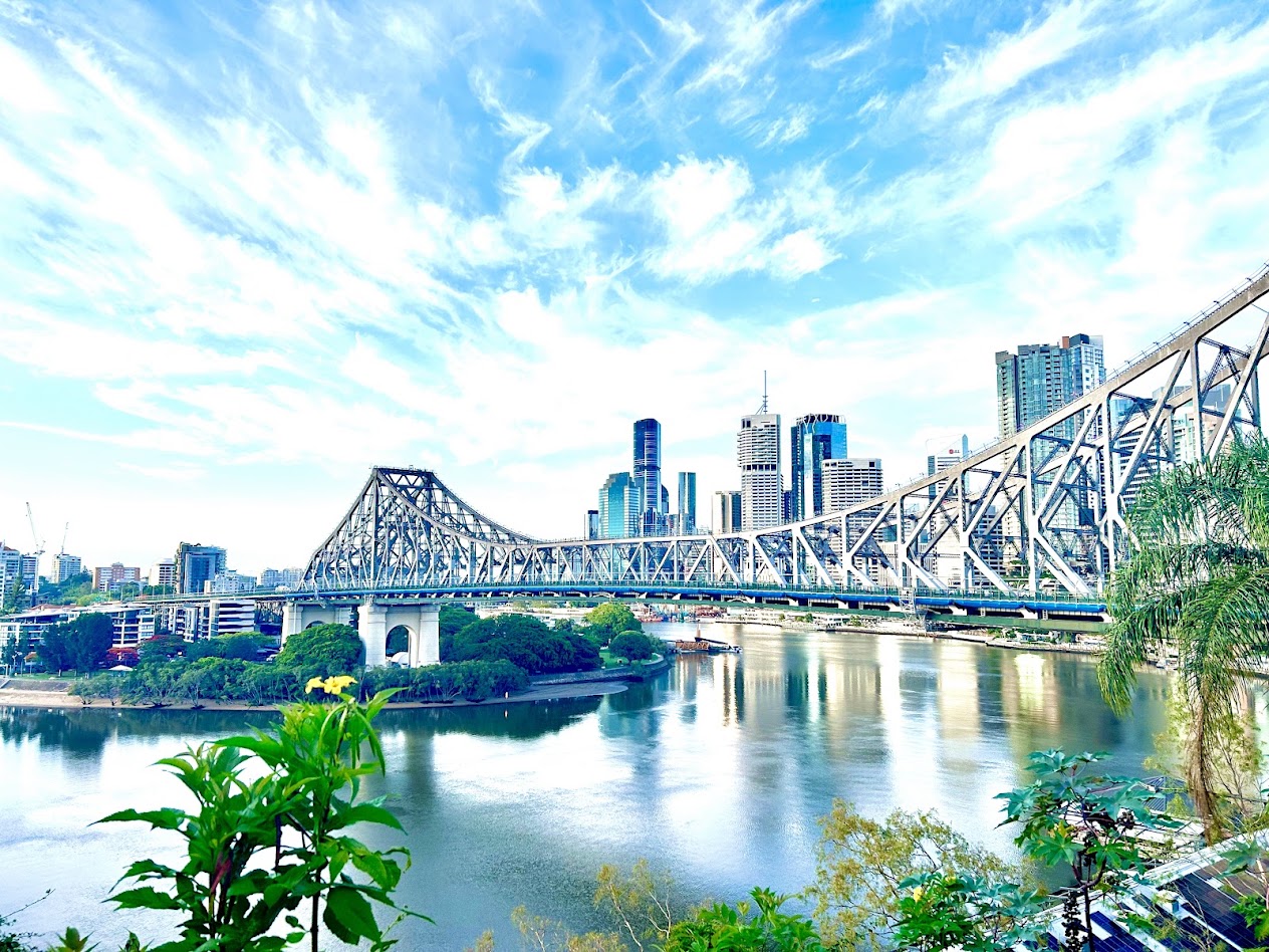 A sweeping view of a steel bridge, city skyline and river beneath a bright blue sky